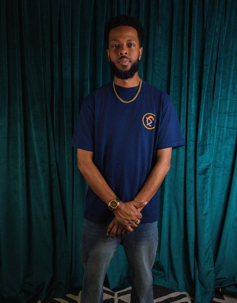 Man wearing a navy shirt standing with hands clasped in front of green velvet curtain in Dungeon Forward - Once Upon - Midnight Premium Tee Shirt